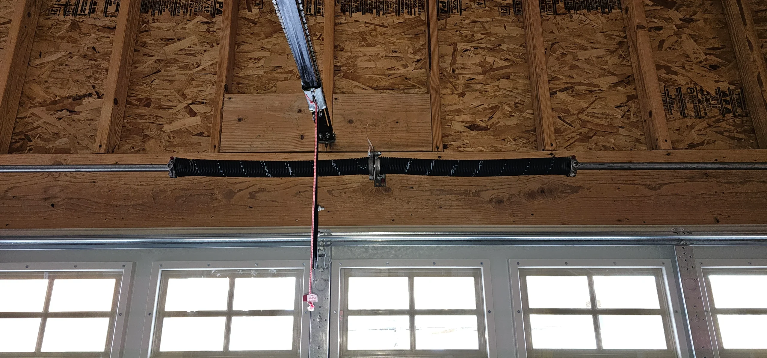 An overhead view of a dual torsion spring assembly mounted firmly above a windowed garage door header illustrates the exact configuration involved in How to Change Garage Door Springs