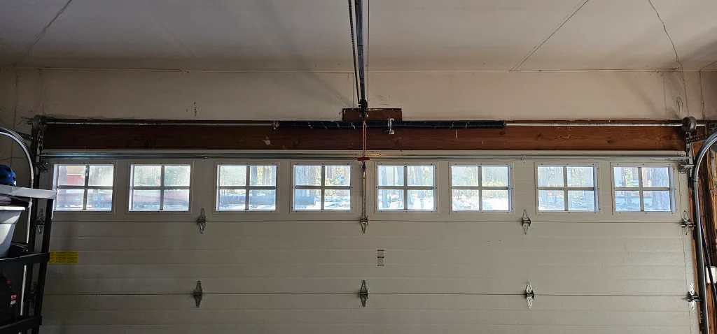 A wide view of a multi-panel, windowed garage door assembly highlights a standard torsion spring configuration mounted horizontally above the upper frame, perfectly capturing the mechanical backdrop for Understanding the Role of Garage Door Springs
