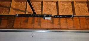 An overhead view of a dual torsion system mounted horizontally to a wood header plate frames the clear mechanical failure in What Skilled Technicians Check During Garage Door Spring Repair.