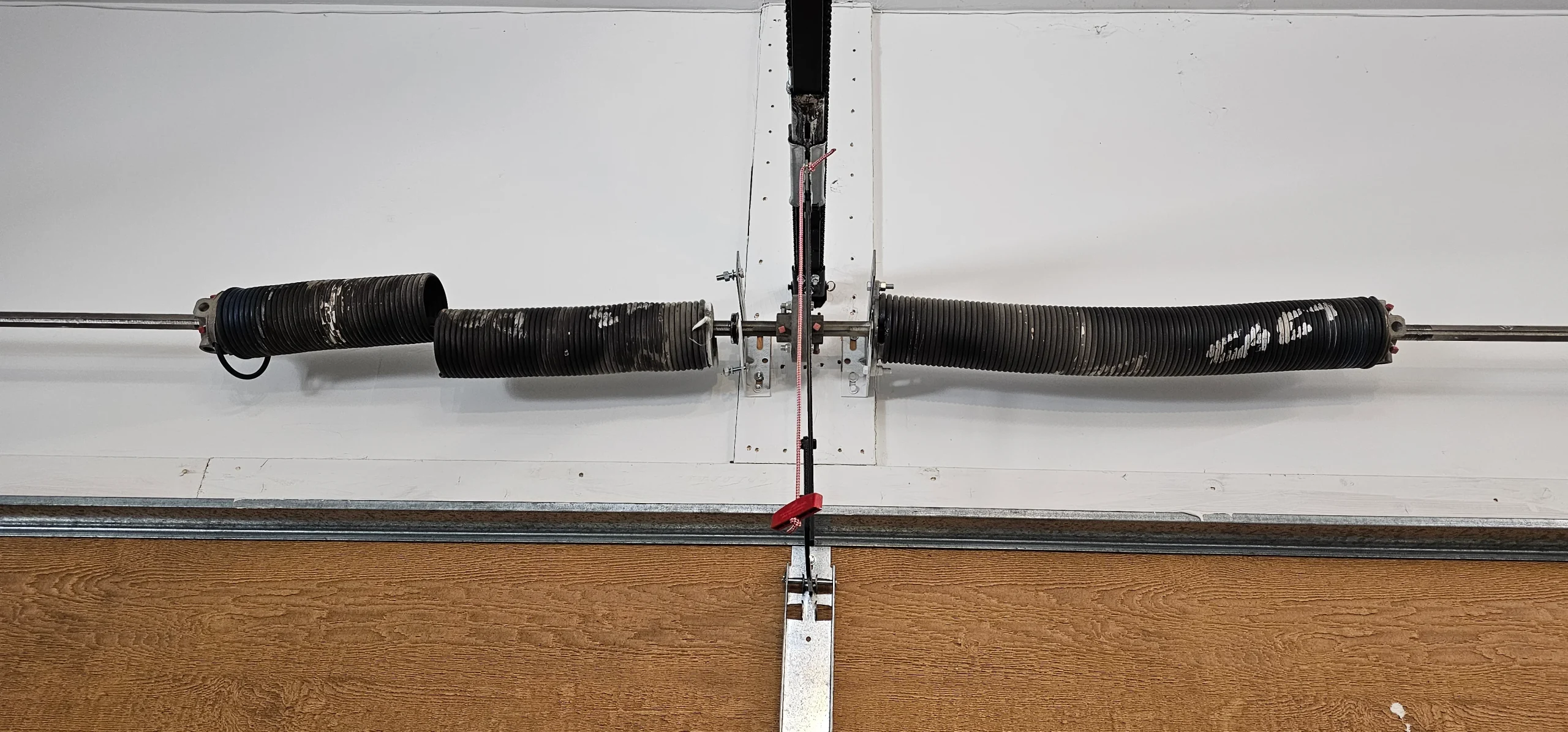 An overhead, close-up view of a broken dual torsion spring assembly cleanly illustrates the structural backdrop for Key Factors That Affect Garage Door Repair Cost