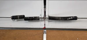 An overhead, close-up view of a dual torsion system horizontally mounted above a garage door panel perfectly illustrates the physical aftermath of a component failure in What Happens When Garage Door Springs Break