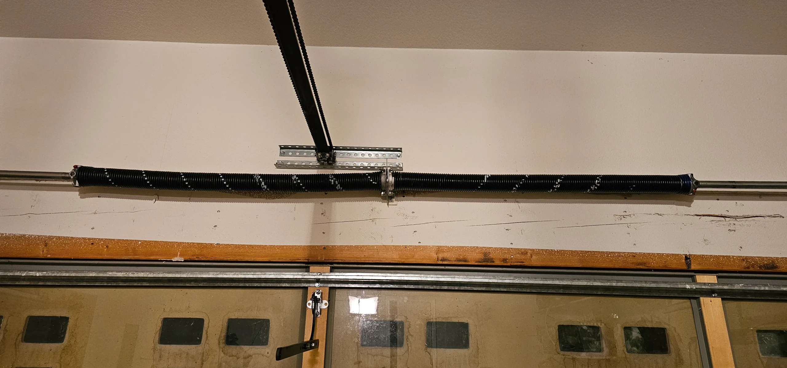 An overhead view of a clean, fully intact dual torsion spring assembly mounted above a sectional door panel frames the ideal standard for Garage Door Spring Maintenance.