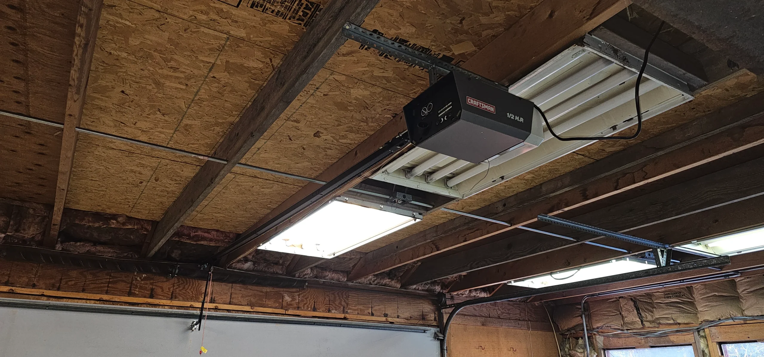 An interior view of a classic Craftsman $\text{1/2 HP}$ chain or belt drive garage door opener mounted to a raw, exposed wood rafter ceiling captures the exact mechanical centerpiece featured in Most important garage door feature.